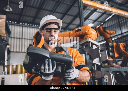 Team di tecnici addetti alla manutenzione della saldatura robotizzata che lavora nello stabilimento di automazione. Un lavoratore maschio aziona il controller manuale del software del braccio robotico nella produzione automatizzata Foto Stock