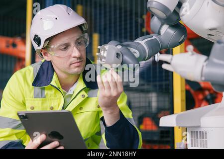 ingegnere professionista maschio caucasico che lavora con il braccio robotico automatizzato per la moderna tecnologia industriale di fabbrica Foto Stock