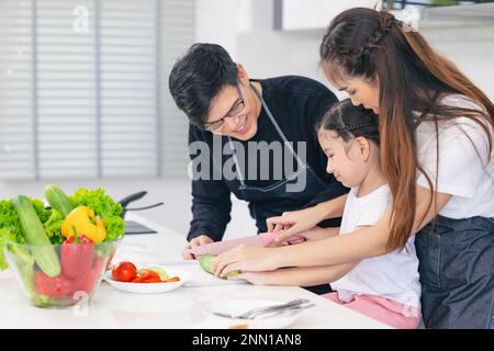 Bambino che gioca il cibo del cuoco con il padre e la madre nella cucina domestica. Momenti asiatici di felicità della famiglia insieme. Foto Stock