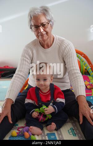 Ritratto bambino seduto sul pavimento a giocare con la nonna a casa Foto Stock