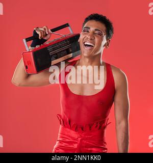 Radio Happy, uomo e boombox in studio per gay, orgoglio e moda estetica con retrò 80s tecnologia da sfondo rosso. Modello LGBTQ, moda vintage e. Foto Stock