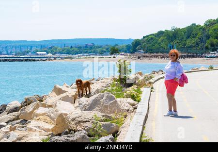 Senior elegante 73 anni donna divertirsi con il suo cocker spaniel maschio animale domestico su una passeggiata nella bella giornata di primavera a Varna Beach Promenade, Bulgaria, maggio 2022 Foto Stock