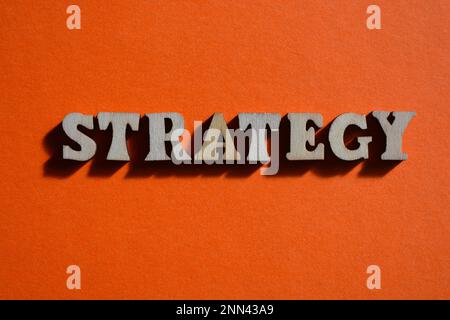 Strategia, parola in lettere alfabetiche di legno isolate su sfondo arancione Foto Stock