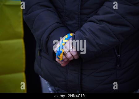 Pamplona, Spagna. 24th Feb, 2023. Una persona che tiene un braccialetto con la bandiera Ucraina. La popolazione Ucraina si è riunita nella piazza del castello di Pamplona in occasione del primo anniversario della grande invasione russa dell'Ucraina. Credit: SOPA Images Limited/Alamy Live News Foto Stock