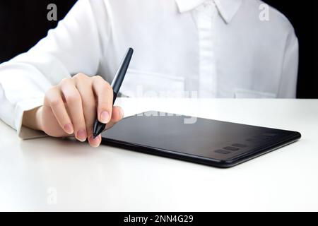 Una giovane ragazza lavora su un tablet grafico wireless, tenendo una penna in una mano. Foto Stock