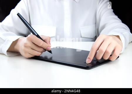 Una giovane ragazza lavora su un tablet grafico wireless, tiene una penna in una mano e preme un pulsante con l'altra Foto Stock