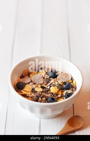 ciotola per la colazione con avena, mais e fiocchi e frutti di bosco freschi sul tavolo di legno bianco, spazio copia Foto Stock