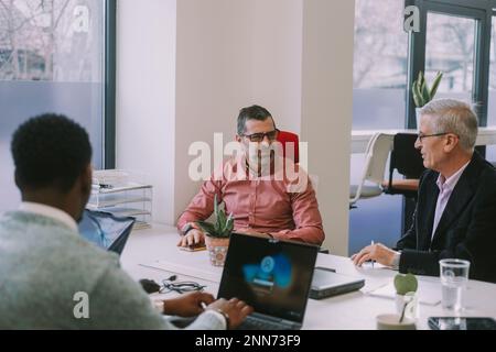 Uomini d'affari anziani che hanno una conversazione mentre sono seduti alla scrivania presso il co-spazio di lavoro Foto Stock