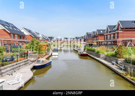 Moderne case in mattoni a basso consumo energetico con pannelli solari sul tetto lungo un canale nei Paesi Bassi in una giornata di sole estate Foto Stock