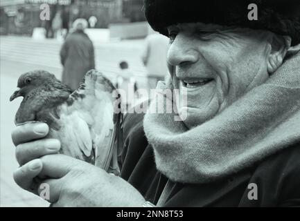 Nero e bianco sorridente vecchio volto guardando con speranza e tenerezza ad un piccione spaventato. Foto Stock