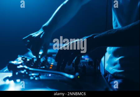 Mani di un DJ mixare brani musicali con il mixer audio. Primo piano foto del disco di gioco di jockey ambientato sul palco nel night club Foto Stock