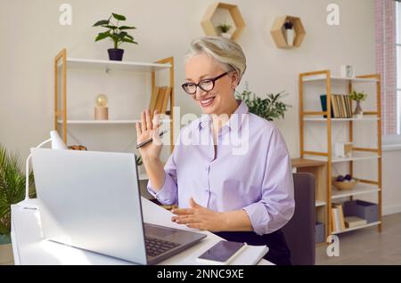 Una donna anziana dai capelli grigi con un sorriso sul viso usa un notebook per comunicare. Foto Stock