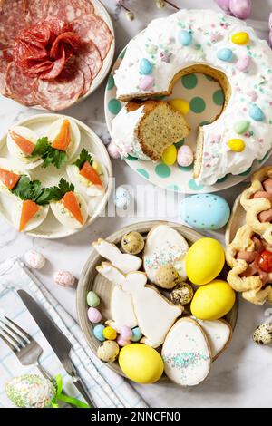 Cena festiva, brunch di Pasqua. Scena di Pasqua con un assortimento di cottura, dessert, uova farcite e uova tinte su uno sfondo di marmo. Visualizza da Foto Stock