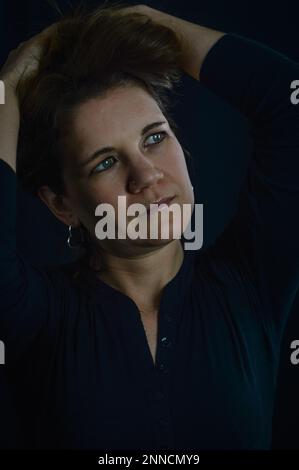ritratto di una bella donna bionda che tiene i capelli sopra la testa e che guarda via nostalgicamente Foto Stock