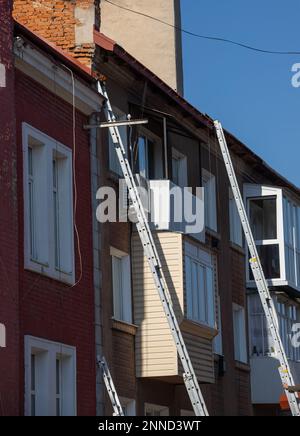 Una scaletta di prolunga si appoggia alla parte anteriore di un edificio con alloggiamento multiplo in preparazione delle riparazioni del tetto. Foto Stock