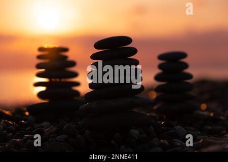 Profilo equilibrato piramidale di ciottoli sulla spiaggia al tramonto con Mare sullo sfondo. Pietre Zen sulla spiaggia di mare, meditazione, spa, armonia, calma, Foto Stock