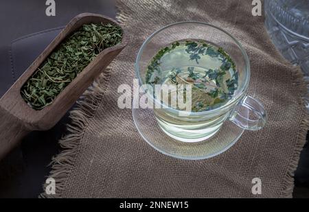 Rinfrescati e gusta una tazza di tè alla canapa calda (tè alle erbe CBD) a partire da foglie di canapa organica essiccate in una paletta di legno sulla placemat di burlap. Bevanda sana conc Foto Stock