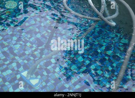 Uomo pulizia piscina con aspirapolvere. Manutenzione settimanale della piscina. Servizio di pulizia della piscina. Foto Stock
