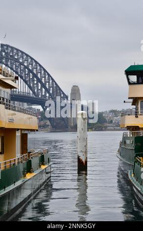 Sydney Harbour Bridge visto attraverso due iconici traghetti pendolari gialli e verdi a Circular Quay con acque calme e pianeggianti Foto Stock