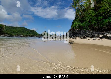 Le morbide spiagge di sabbia bianca di Amanave, sull'isola di Tutuila, Samoa Americane, con le lussureggianti montagne verdi e le formazioni rocciose. Foto Stock