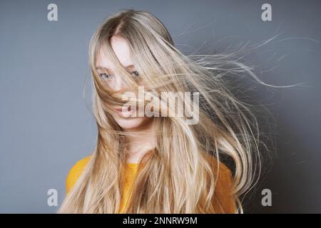 Giovane donna bionda con lunghi spazzate dal vento capelli tousled soffiaggio dentro il suo volto Foto Stock