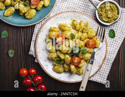 Gnocchi in piatti con pesto verde, pomodori ed erbe su fondo rustico di legno, primo piano, vista dall'alto. Piatti tradizionali della cucina italiana Foto Stock