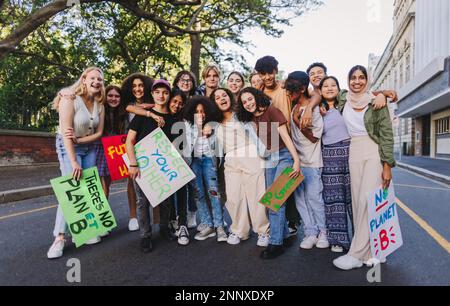 Un gruppo di attivisti giovanili diversi sorride allegro mentre si riunisce in una protesta contro il cambiamento climatico. I giovani multiculturali si uniscono al mondo Foto Stock