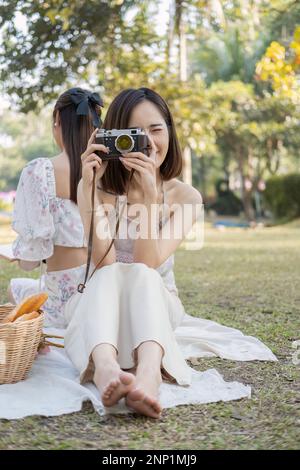 Bella bella donna asiatica in abiti casual si siede sul vestito da picnic, tenendo una macchina fotografica, sorridendo e guardando nella macchina fotografica Foto Stock