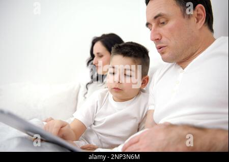 famiglia, paternità, tecnologia e gente concedono buon padre e piccolo figlio con un pc tablet seduto sul divano di casa. mamma donna che lavora in background online sul computer portatile Foto Stock