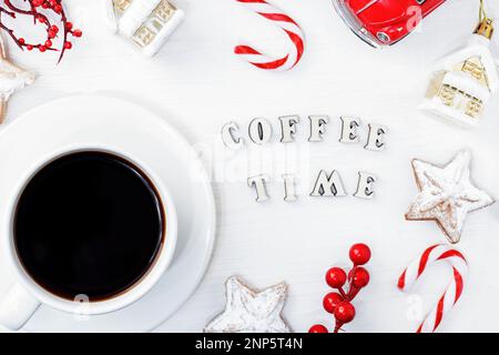 Una tazza bianca di caffè americano nero su uno sfondo di legno bianco accanto ai biscotti di Natale, una canna da zucchero e i giocattoli di Capodanno. Testo tempo caffè Foto Stock