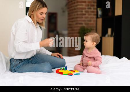 Mamma che misura la temperatura al bambino con il termometro, seduto a letto in camera da letto, spazio libero Foto Stock