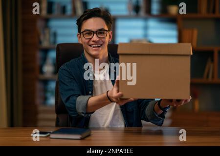 Giovane uomo eccitato seduto alla scrivania, tenendo in mano la scatola di consegna Foto Stock
