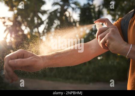 L'uomo sta applicando repellente per insetti sulla sua mano contro le palme. Prevenzione contro morso di zanzara in destinazione tropicale. Foto Stock