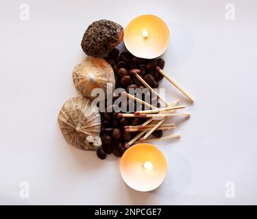 Un mucchio di chicchi di caffè è circondato da conchiglie e da una pietra vulcanica. I fiammiferi sono posti sui chicchi di caffè e due candele sono sul lato. Foto Stock