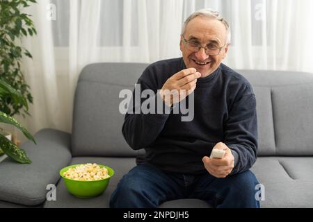 Ritratto dell'uomo anziano che guarda la TV con popcorn e un telecomando Foto Stock