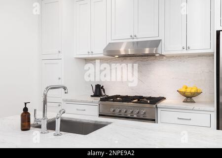 Un particolare cucina con armadi bianchi, stufa in acciaio inossidabile e cappuccio, ripiani in marmo e backsplash, e un lavello cromato. Foto Stock