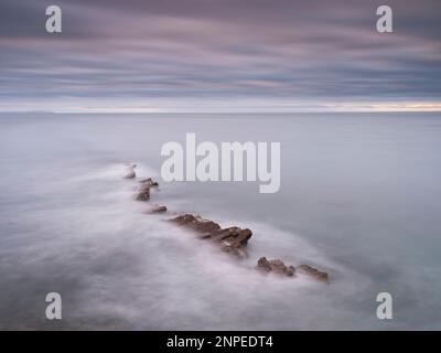 Onde che si lavano da una sporgenza rocciosa a Peveril Point. Foto Stock