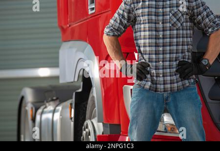 Primo piano del conducente caucasico maschio del camion in piedi davanti al primo piano del trattore semi-camion. Tema del trasporto. Foto Stock