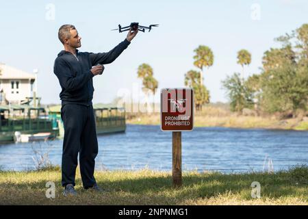 L'uomo volerà il suo quadricottero in nessuna zona del drone. L'operatore utilizza illegalmente il proprio sistema UAS in un parcheggio di stato vicino al segnale di restrizione. Foto Stock