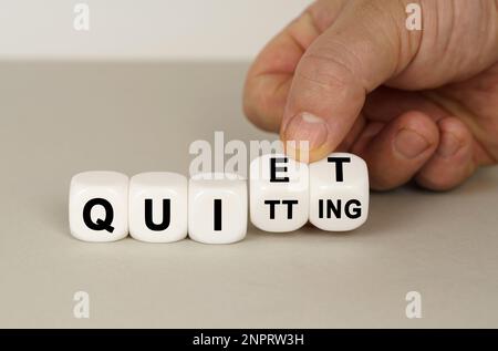 Su una superficie grigia ci sono dei cubi bianchi con l'iscrizione - QUIET o QUITTING. Due dadi in mano. Concetto aziendale. Foto Stock