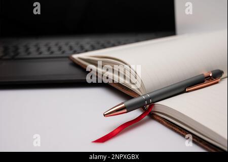Un notebook aperto con un computer portatile e una penna su un desktop che si adatta a un ufficio domestico o a una scrittura creativa. Foto Stock