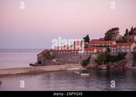 Vista panoramica di Sveti Stefan in Montenegro al tramonto rosa. Famoso luogo turistico vicino a Budva. Bellissima isola naturale, con tetti in terracotta tra i due Foto Stock