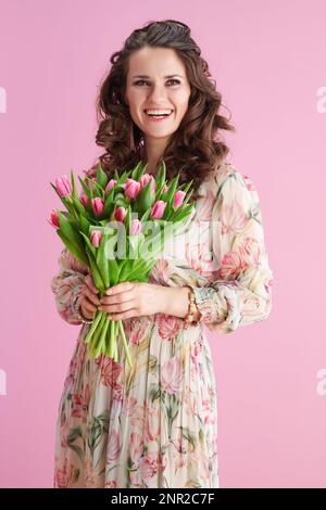 felice donna elegante con lunghi capelli di brunetta ondulata con bouquet di tulipani su sfondo rosa. Foto Stock