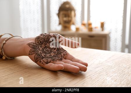 Donna con tatuaggio all'henné sul palmo della mano a tavola all'interno, primo piano. Tradizionale ornamento di mehndi Foto Stock