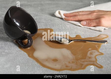 Donna che pulisce il caffè versato sul tavolo grigio, primo piano Foto Stock