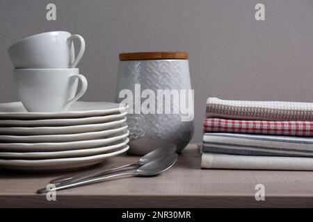 Pila di morbidi asciugamani da cucina e stoviglie su tavolo di legno su sfondo grigio Foto Stock