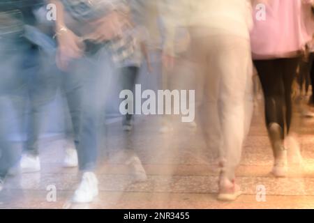 Persone che camminano sotto un portico storico in Italia (Bologna), con abiti colorati e sfocatura del movimento. Camicia a scacchi e felpa con cappuccio rosa sotto il vento caldo. Foto Stock