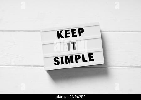 Keep it simple text su lightbox segno, minimo lay piatto design bianco su sfondo di legno, semplicità o concetto minimalista Foto Stock