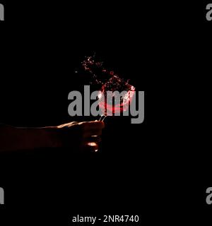 la mano della persona che tiene il vetro il vino rosso che spruzzi fuori il vetro. Foto ad alta risoluzione Foto Stock