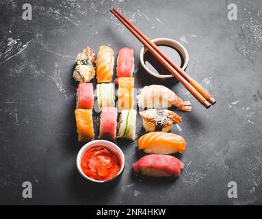 Vista dall'alto del sushi giapponese assortito con panini, nigiri, salsa di soia, zenzero, bacchette su fondo di cemento nero. Cena o pranzo asiatico Foto Stock